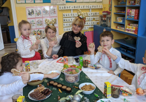 Uroczystość Wigilijna w klasie grupy VI - Dzieci oraz nauczycielka grupy siedząc przy stole pełnym smakołyków składają świąteczne życzenia